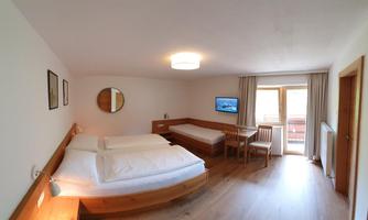 A cozy room with two beds and a table. Large windows provide plenty of daylight and a view outside.