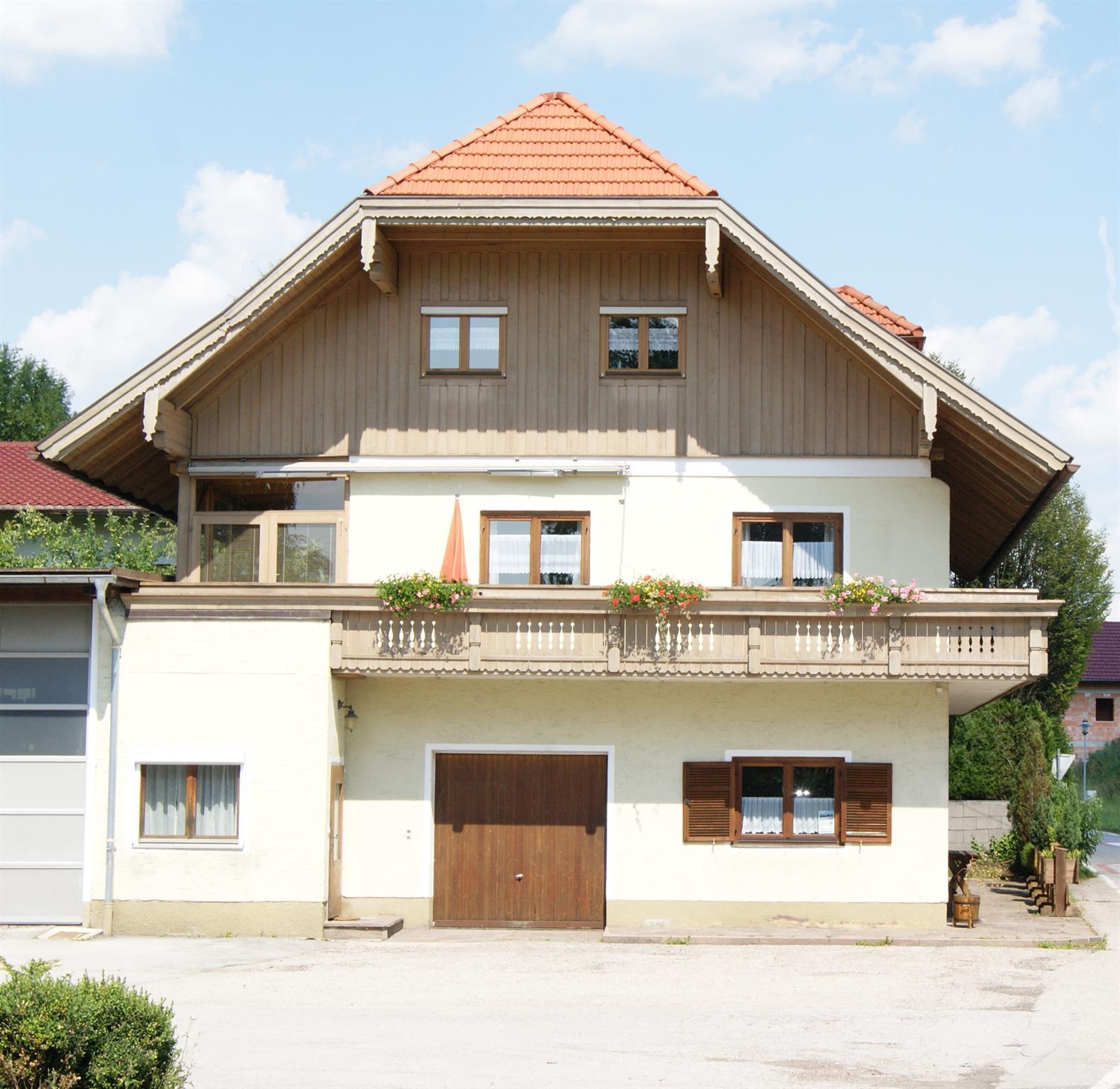 A traditional house with a red roof and wooden details. It has a balcony with flowers and an inviting facade.