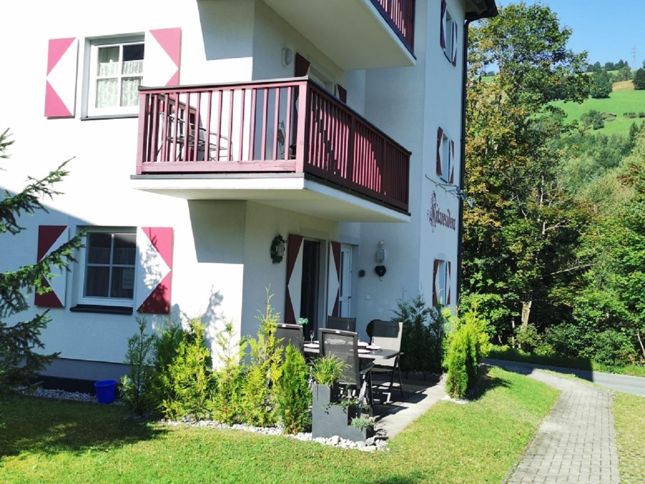 A modern house with a balcony and a cozy terrace. The surroundings are green, surrounded by trees and a well-maintained lawn.