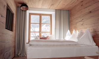 A cozy bedroom with wooden paneling and a large window. The room is bright and modern, with an inviting bed and stylish curtains.