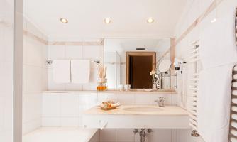 A modern bathroom with white tiles and soft lighting. There is a sink, a large mirror, and fresh towels.