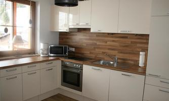 A modern kitchen with light cabinets and a wooden countertop. It is well-equipped with a stove, a microwave, and a sink.