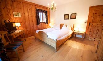 A cozy bedroom with wood paneling and a double bed. There is a desk, two lamps, and a window with curtains.