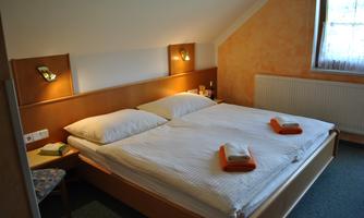 A cozy bedroom with a double bed and a window. The walls are painted in warm colors and there are chairs as well as towels on the bed.