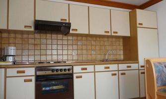 A modern kitchen with bright wooden cabinets and a tiled backsplash. The equipment includes a stove, a sink, and a coffee machine.