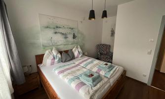 A cozy bedroom with a large double bed and colorful bedding. A beautiful painting hangs on the wall, and the room is bright and inviting.