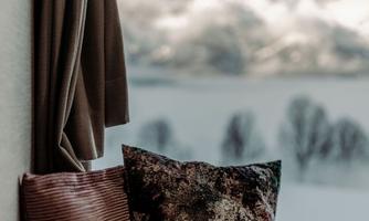 A cozy spot with two cushions in front of a window. In the background, snow-covered mountains can be seen.