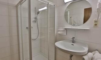 A modern bathroom with a shower cabin and a sink. The walls are brightly tiled, and a round mirror is mounted.
