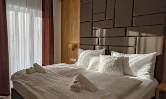 A modern bedroom with a large double bed and elegant wood paneling. Daylight streams through the windows, creating an inviting atmosphere.
