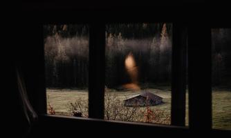 A view from a window onto a rainy landscape with a lonely house and trees in the background. The fog gives the scene a mystical atmosphere.
