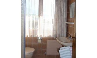 A bright bathroom with a window, a sink, and a shower. The walls are decorated with tiles in warm colors.