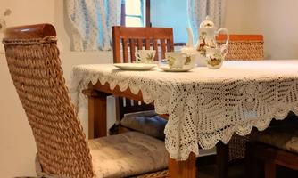 A cozy dining area with a wooden table and woven chairs. On the table are tea utensils and a lace tablecloth.