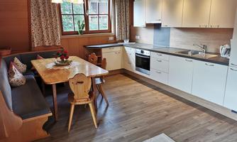A modern kitchen with a dining table and wooden bench. Large windows provide plenty of daylight.