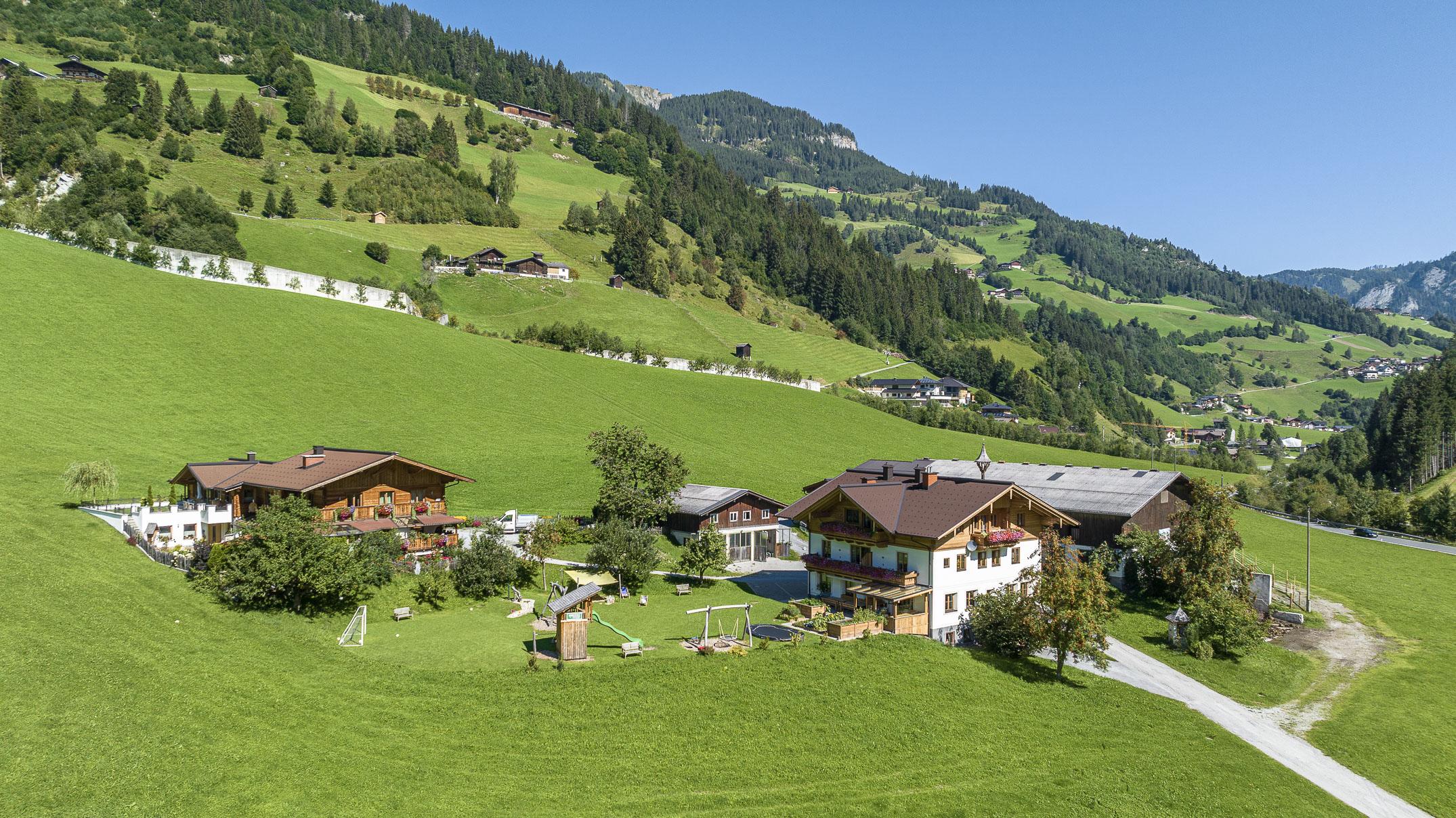 A picturesque mountain landscape with green meadows and a group of traditional houses. The sky is clear and nature appears idyllic and peaceful.