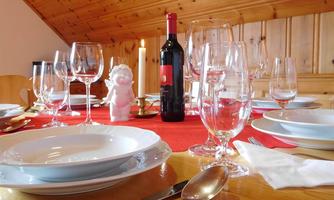 A set table with white plates and various glasses. In the center is a bottle of red wine and a candle holder.