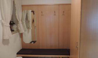 A simple entryway with a wooden cabinet, a bench, and a mirror. The walls are light, and curtains frame the window.