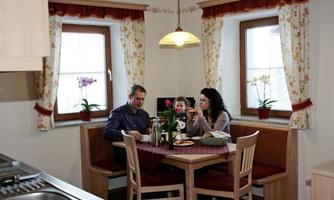 A family is sitting at a dining table in a cozy kitchen. They are enjoying a meal and having a pleasant time together.