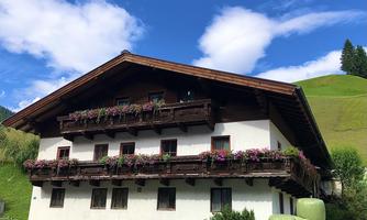 A traditional Bavarian farmhouse with wooden decorations and flower boxes. In the background, there are gentle hills and a blue sky.