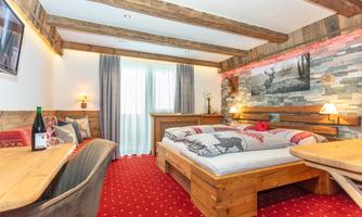 An inviting bedroom with wooden furniture and a red upholstered carpet. The large windows provide plenty of daylight, and the decor radiates coziness.