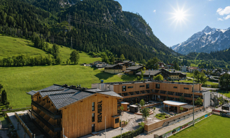A modern hotel is located in a picturesque mountain landscape. The surroundings are green and offer stunning mountain views.