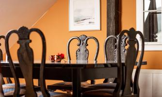A stylish dining area with a black table and elegant chairs. The orange wall and a piece of artwork give the space warmth and character.
