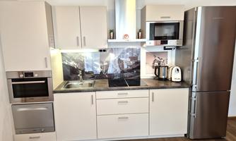 A modern kitchen with white cabinets and stainless steel appliances. There is a stove, a refrigerator, and an elegant countertop.