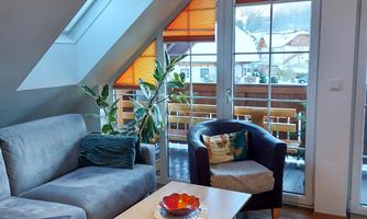 A cozy living room with a gray sofa and a small table. Large windows with orange blinds let in plenty of light.