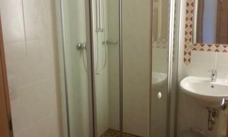 A modern bathroom with a shower cabin, a sink, and a toilet. The walls are light tiled and the floor has a decorative pattern.