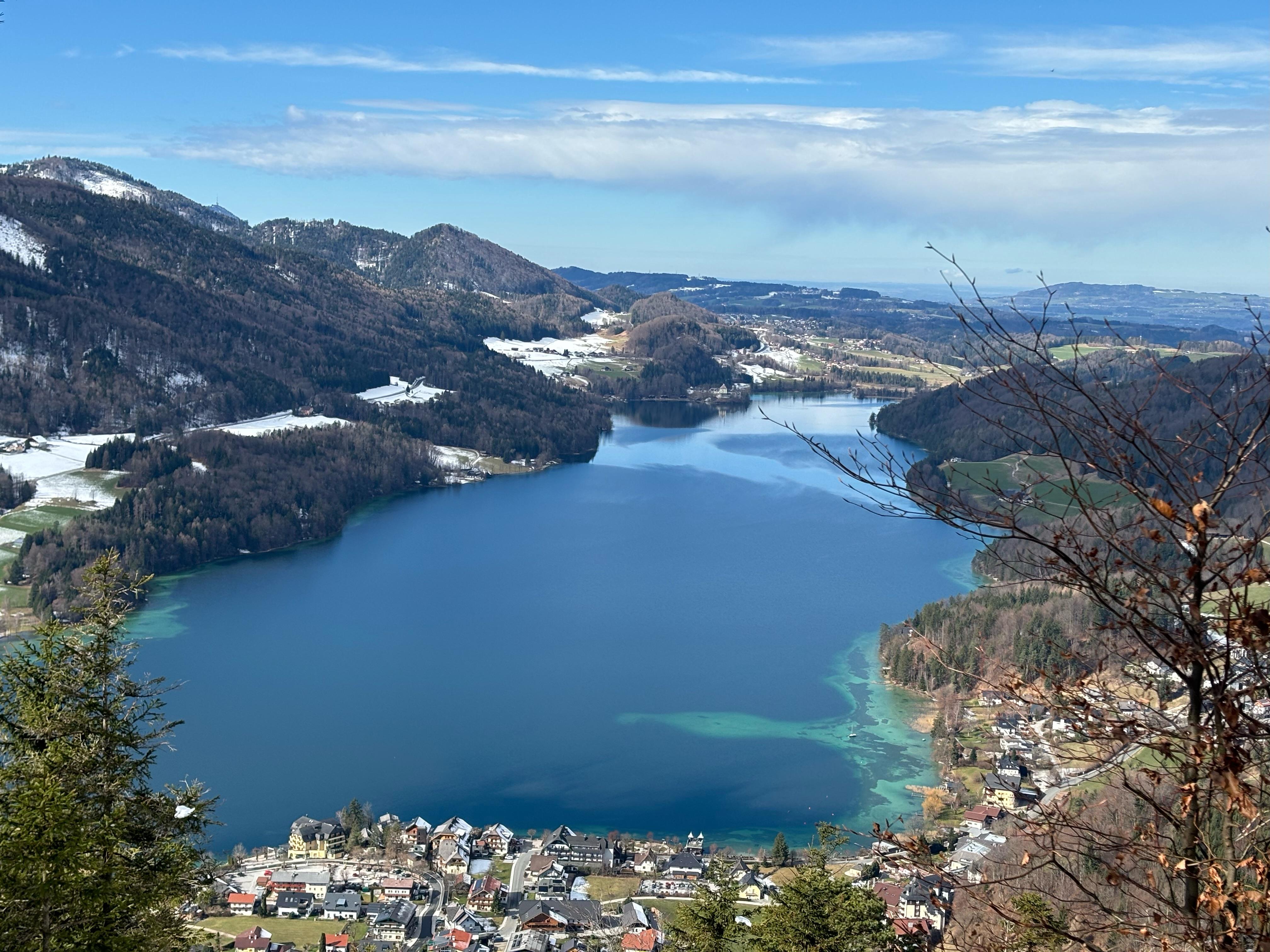 A picturesque view of a lake surrounded by hills and mountains. The landscape features fresh water and green shores.