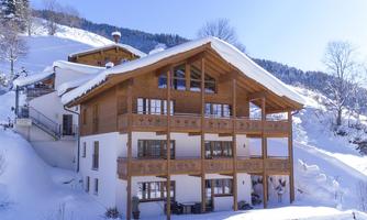 A cozy chalet in the snow, surrounded by mountains. The clear sky makes the winter landscape shine.
