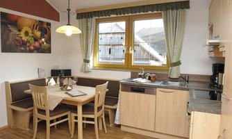 A modern kitchen with a dining table and chairs. Large windows provide plenty of daylight and a cozy atmosphere.