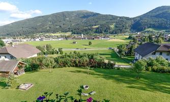 A vast landscape with green meadows and mountains in the background. Small houses line the scene under a clear sky.