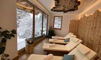A peaceful wellness room with modern loungers and large windows that overlook a snowy landscape. The wood paneling gives the room a cozy atmosphere.