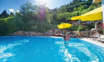 A beautiful pool surrounded by trees and colorful umbrellas. The sun is shining, creating a relaxed atmosphere.
