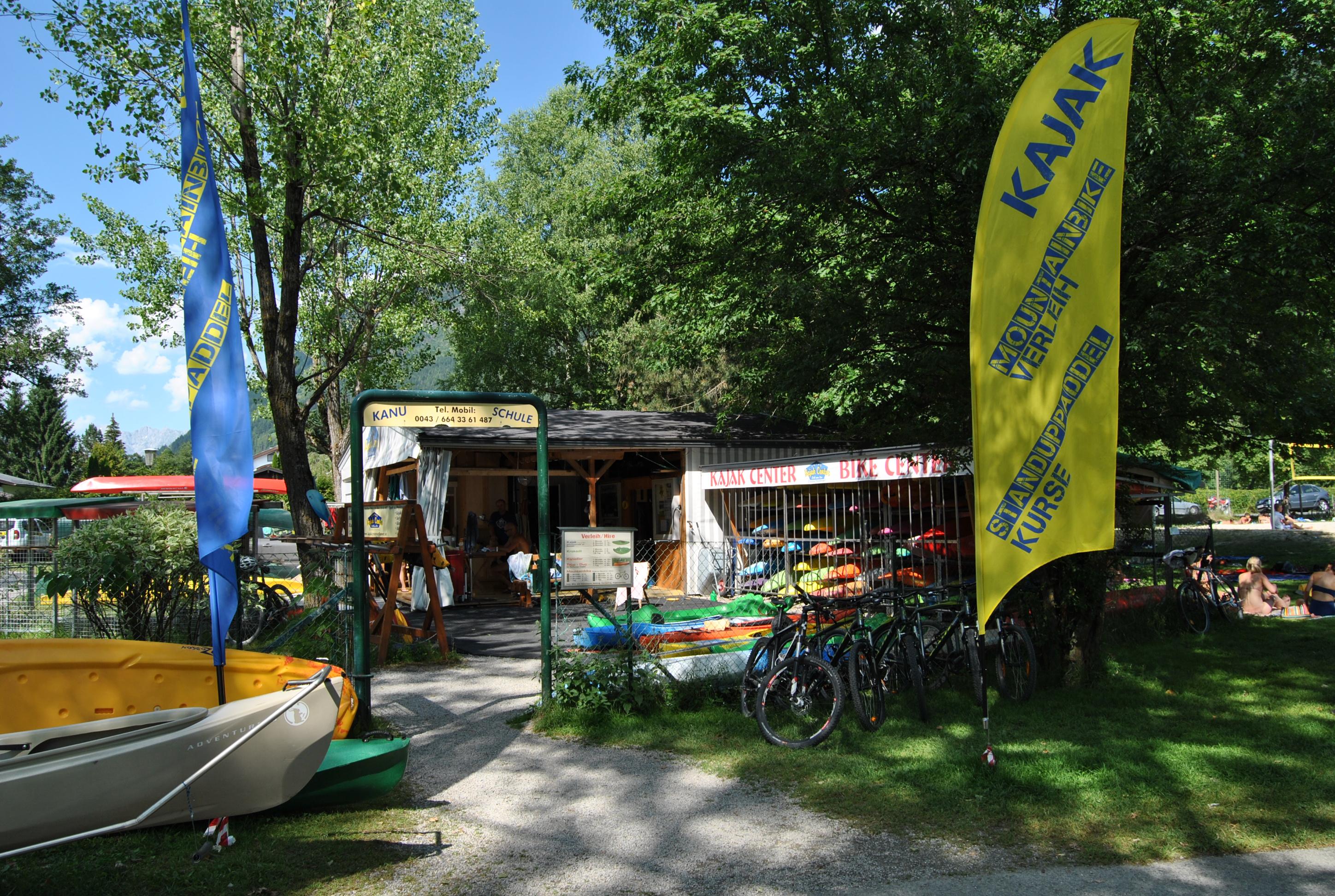 A kiosk by the lake with a yellow flag and several bicycles. The surroundings are green and inviting, ideal for recreational activities.