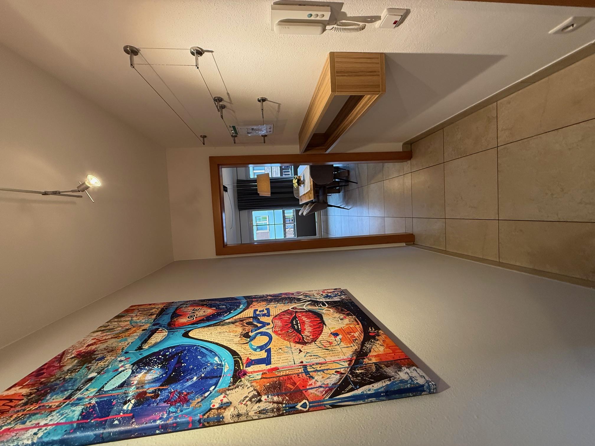 A modern hallway with a colorful piece of artwork on the wall. The room is bright and leads to a cozy dining area.