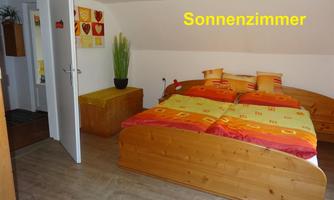 A cozy bedroom with a double bed and colorful bedding. A plant and wooden furniture give the room a warm atmosphere.
