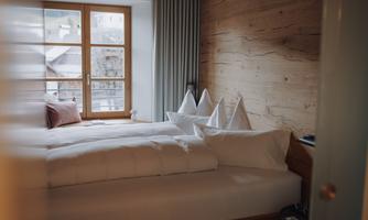 A cozy bedroom with two beds and a large window. The walls are made of wood, and the decoration is simple and modern.