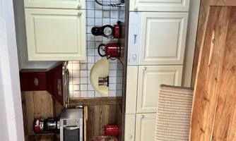 A modern kitchen with light cabinets and a red extractor hood. On the countertop, various kitchen appliances and a sink can be seen.