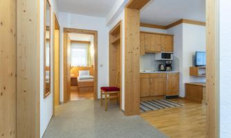 A bright hallway with wood paneling and several doors. On the left side, there is a kitchen and a living area.