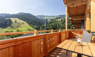 A beautiful balcony with a wooden railing and a view of green mountains. The sun is shining and the landscape is idyllic.
