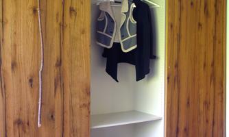 A modern wardrobe with wooden fronts. Inside, there are various pieces of clothing hanging and several shelves.