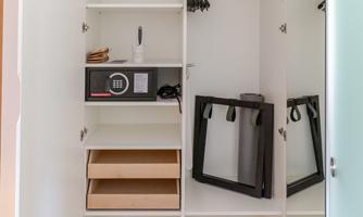 An open wardrobe with a safe, shelves, and a suitcase stand. The wardrobe is neatly and modernly designed.