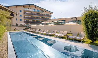 A modern pool area with loungers and sun umbrellas. In the background, there is an elegant building.