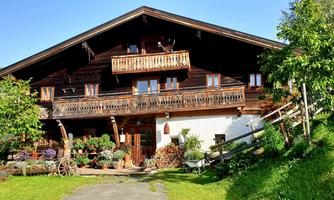 A traditional wooden house with balconies and many plants. In the background, there is a green landscape with mountains.