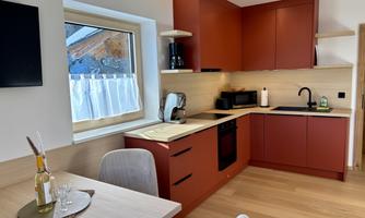 A modern kitchen with red cabinets and wooden surfaces. A table with glasses and a bottle of oil is in the foreground.