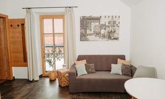 A modern living room with a gray sofa and a small table. Large windows provide plenty of light and a cozy atmosphere.