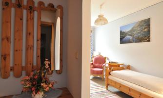 A cozy hallway with wood paneling and a mirror. In the background, you can see a bright room with a bed and a chair.
