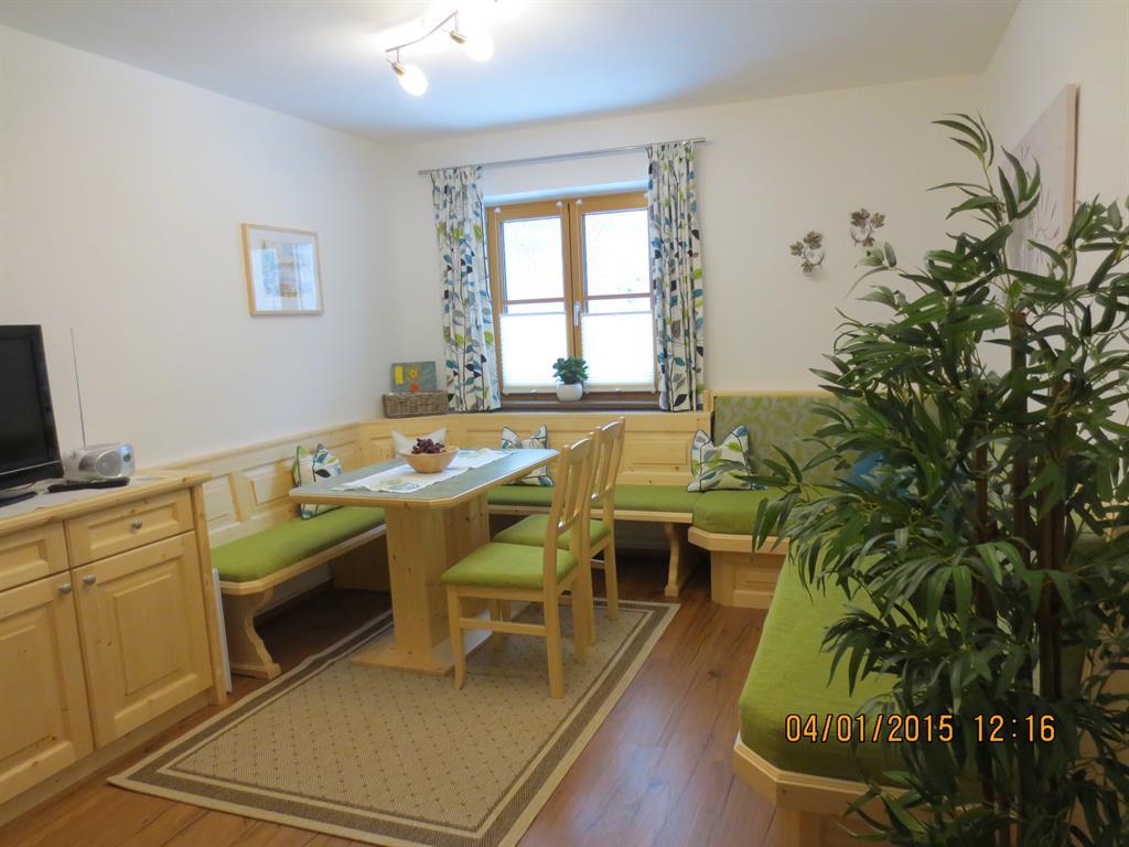 A cozy living space with wooden furniture and a dining set. Bright walls and windows with colorful curtains create a friendly atmosphere.
