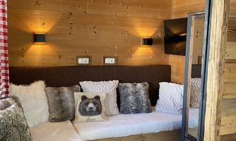 A cozy room with wooden walls and a bright sofa. Cozy cushions and soft lighting create an inviting atmosphere.